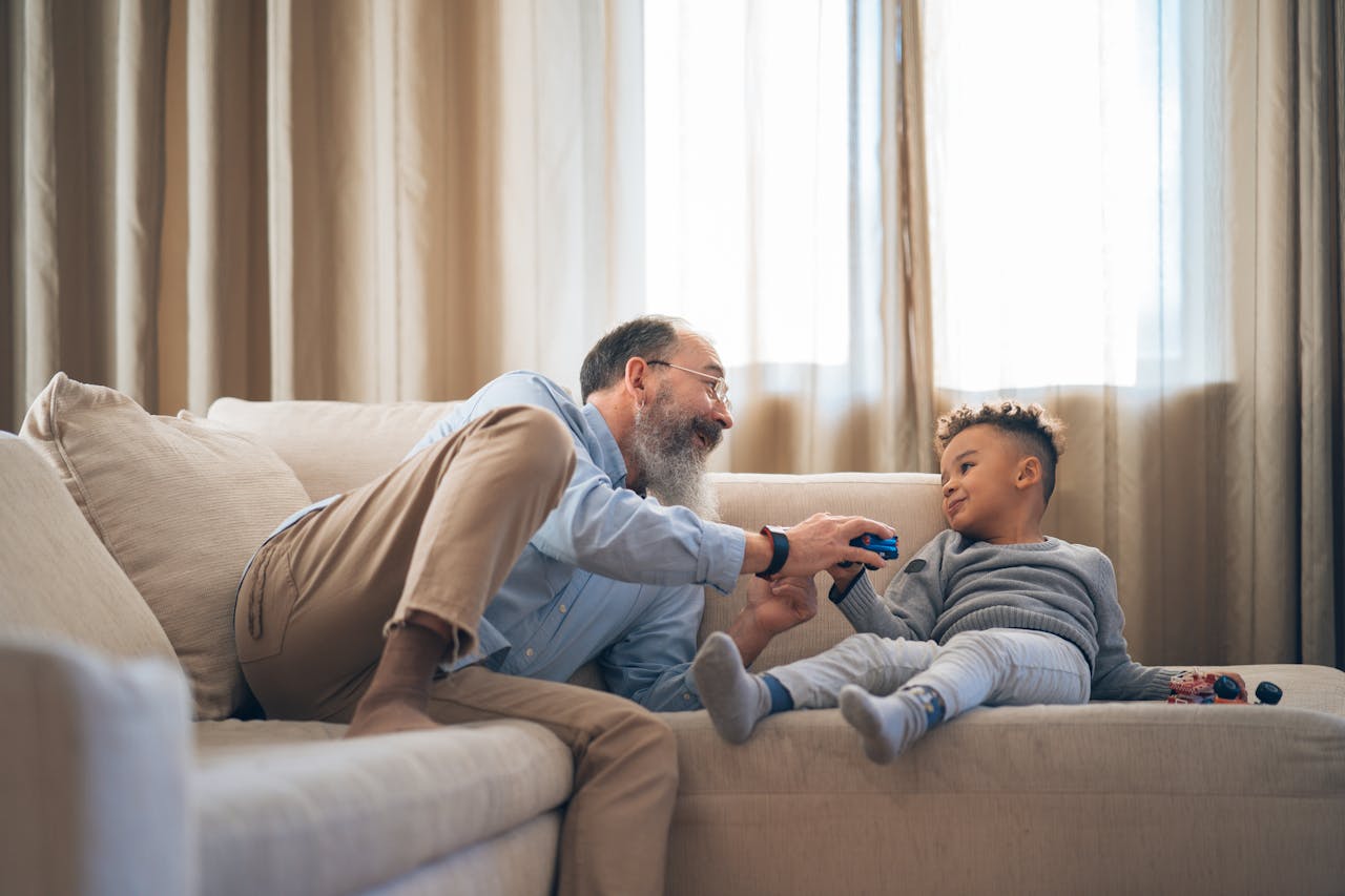 Home A heartwarming moment between grandfather and grandson laughing and playing on a cozy sofa indoors.