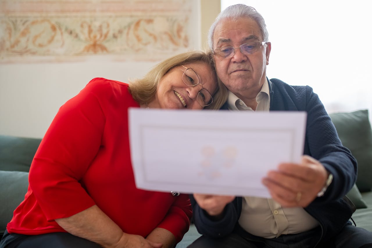 Services An elderly couple happily reviews a document while sitting comfortably together on a sofa.